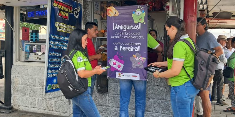 Promotoras de la Empresa de Aseo de Pereira conversan con comerciantes del sector junto a un afiche de la campaña «Juntos cuidamos a Pereira»